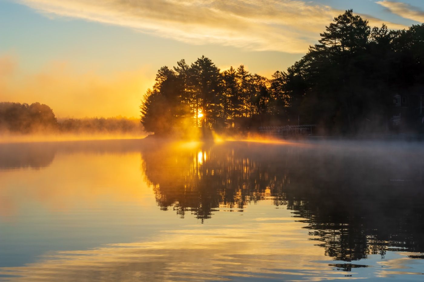 Golden sunrise over a calm, misty lake.