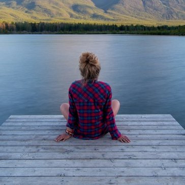 A woman sitting at the end of a dock, looking out over a calm lake.