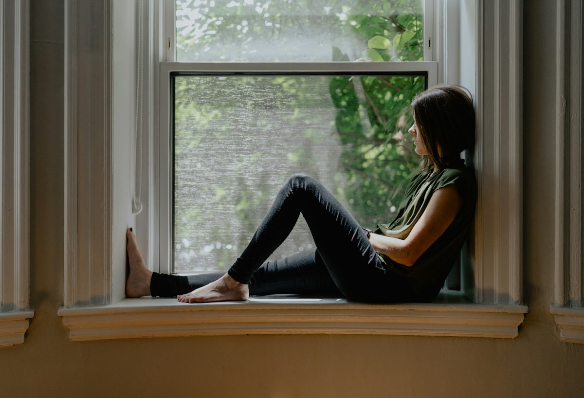 A woman sitting on a sunlit window sill, looking outside.
